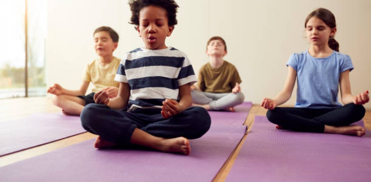 Group Of Children Sitting On Exercise Mats And Meditating In Yoga Studio